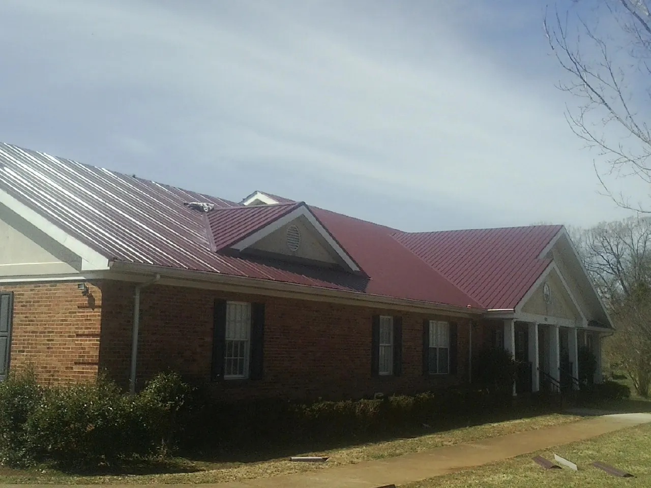 Red metal roof with gabled entries on a long brick building, from a Hail Damage Roof Repair job in Kissimmee