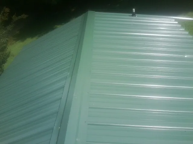 New green metal panels meeting at the ridge of a roof — Flat Roof Repair work by our crew in Kissimmee