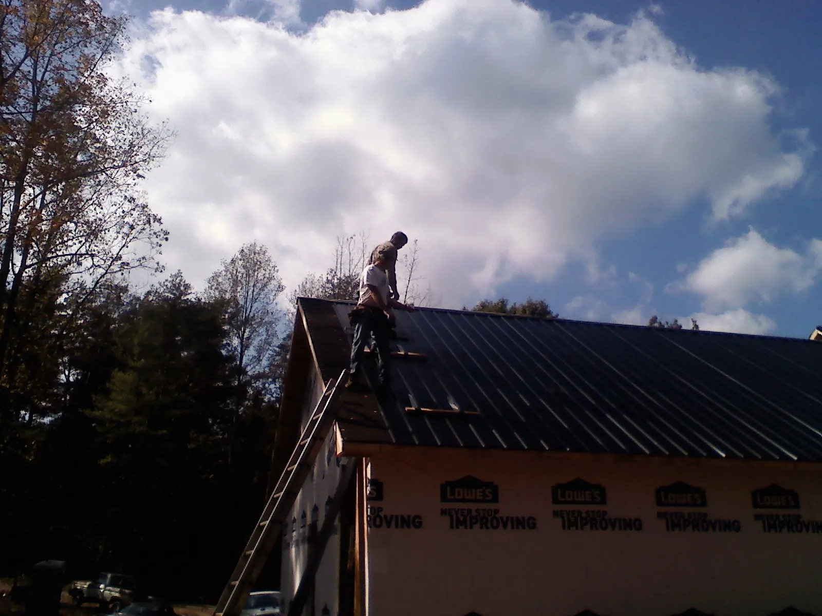 Roofer fastening dark metal panels high against a cloudy sky, from a Roof Inspection job in Kissimmee