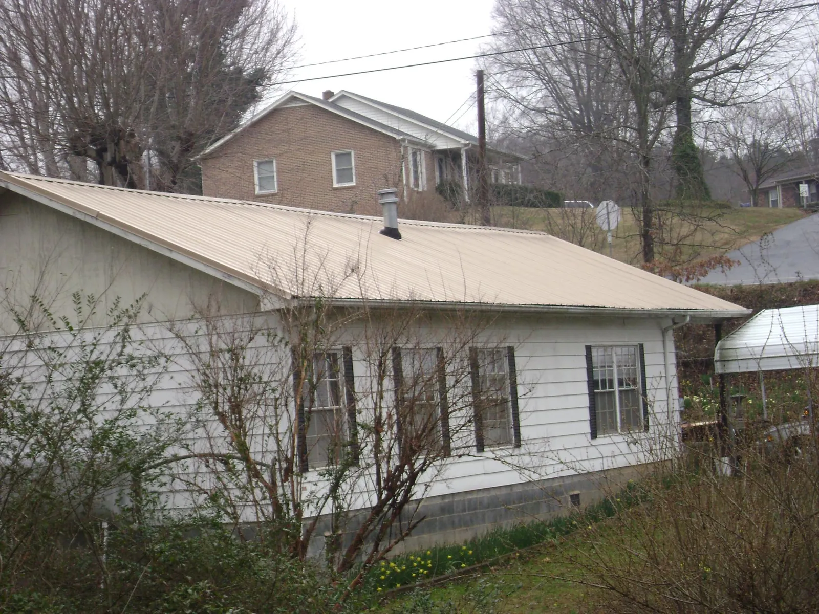 Tan metal roof on a white sided house set into a hillside — Commercial Roofing by Roofing Brothers in Kissimmee